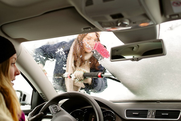 Frau entfernt den Schnee von der Windschutzscheibe eines Autos