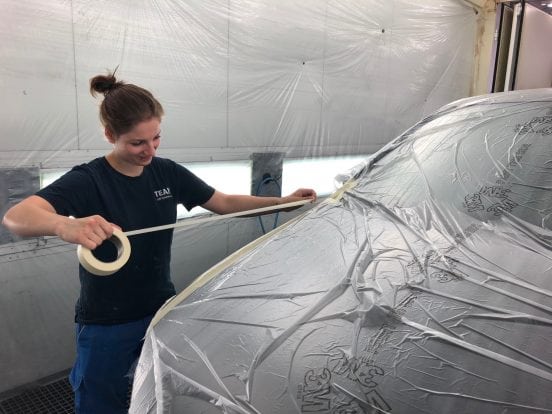 Isabella Joss prépare un véhicule pour les travaux de peinture en recouvrant des parties avec du film et du ruban adhésif.