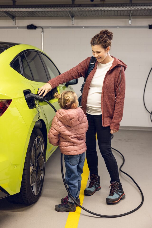 Frau und Mädchen stehen am Elektroauto und laden es auf