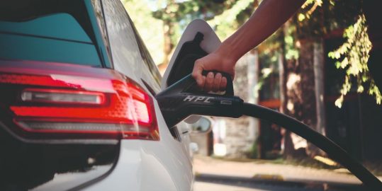 Nahaufnahme einer Hand, die ein Ladekabel in die Ladebuchse eines Elektroautos einsteckt.