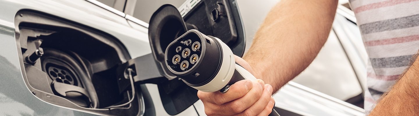 Une main tient une prise de charge, prête à être branchée sur la prise de charge ouverte d'une voiture électrique.