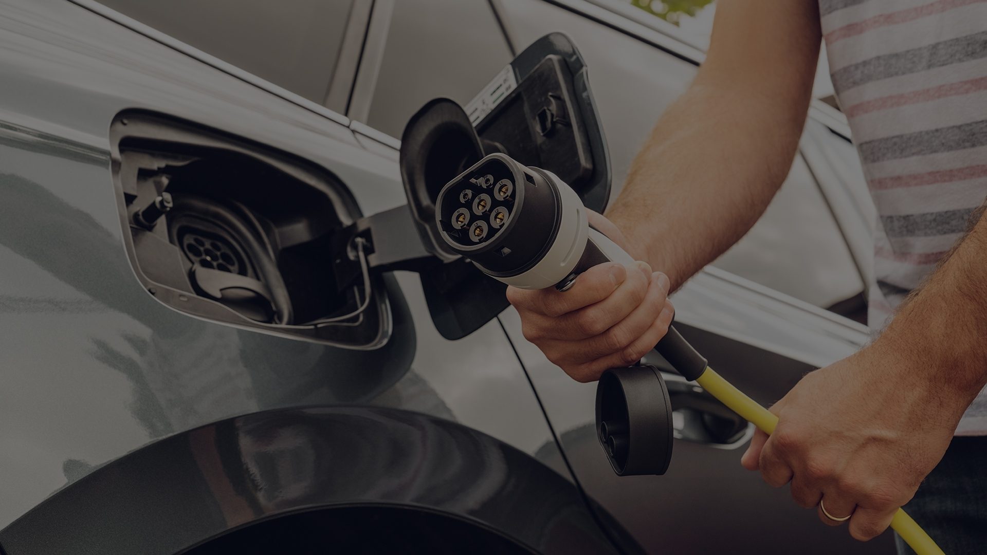 Eine Hand hält einen Ladestecker, bereit, ihn in den geöffneten Ladeanschluss eines Elektroautos zu stecken.